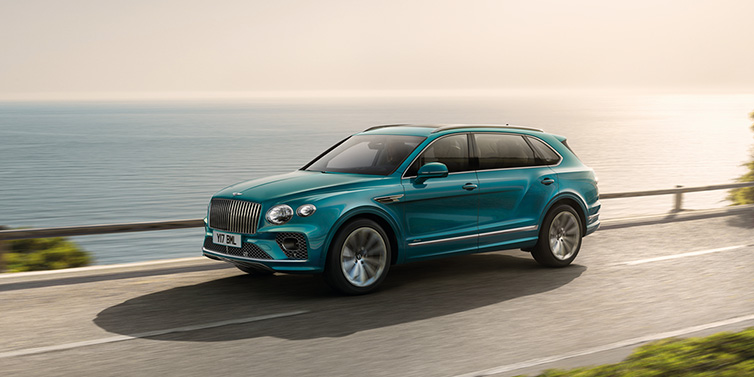 Bentley Busan Bentley Bentayga Extended Wheelbase Azure SUV in Topaz blue paint driving dynamically by the ocean